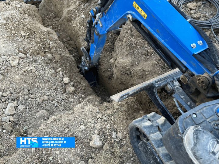HTS Erdbewegung beim präzisen Ausheben einer schmalen Leitungskünette mit Minibagger für die Verlegung von Versorgungsleitungen im Garten.