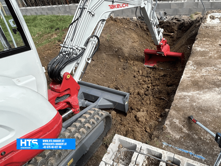 Minibagger beim präzisen Ausheben und Modellieren der zukünftigen Poolfläche entlang einer bestehenden Betonfläche im Garten.