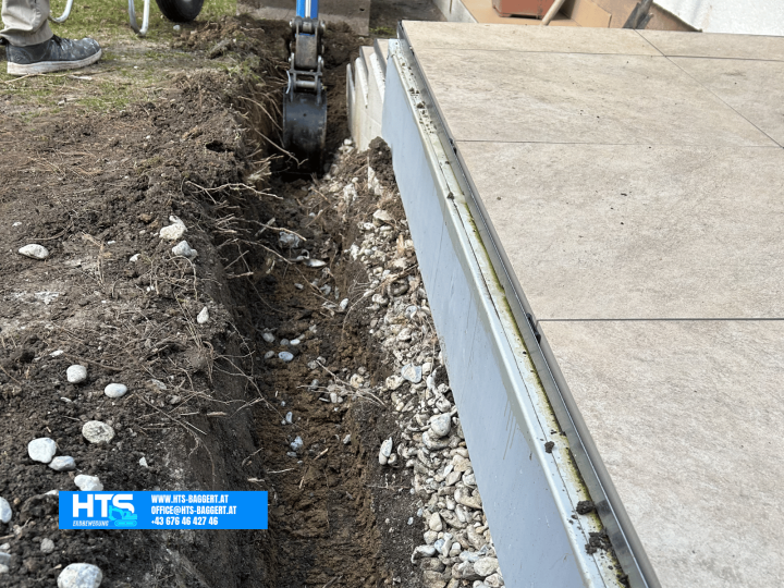 Ausheben einer schmalen Künette direkt neben einer bestehenden Terrasse für die weitere Leitungsverlegung.