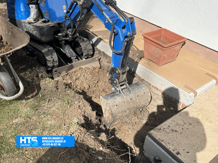 Kompakter Minibagger bei präzisen Erdarbeiten unmittelbar neben einem Wohnhaus bei stark begrenztem Arbeitsraum.