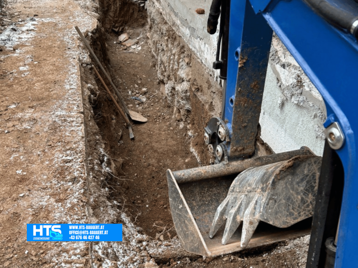 Minibagger beim Aushub entlang der Hauswand zur Vorbereitung einer späteren Drainage am bestehenden Wohnhaus