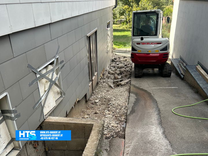 Minibagger im schmalen Arbeitsbereich zwischen zwei Gebäuden bei der Vorbereitung des Bereichs entlang der Hauswand für weitere Erdarbeiten.