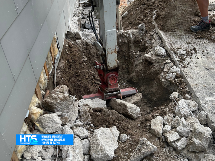Minibagger beim Aushub des Erdreichs direkt entlang der Hauswand für die spätere Trockenlegung und Herstellung einer Drainage.